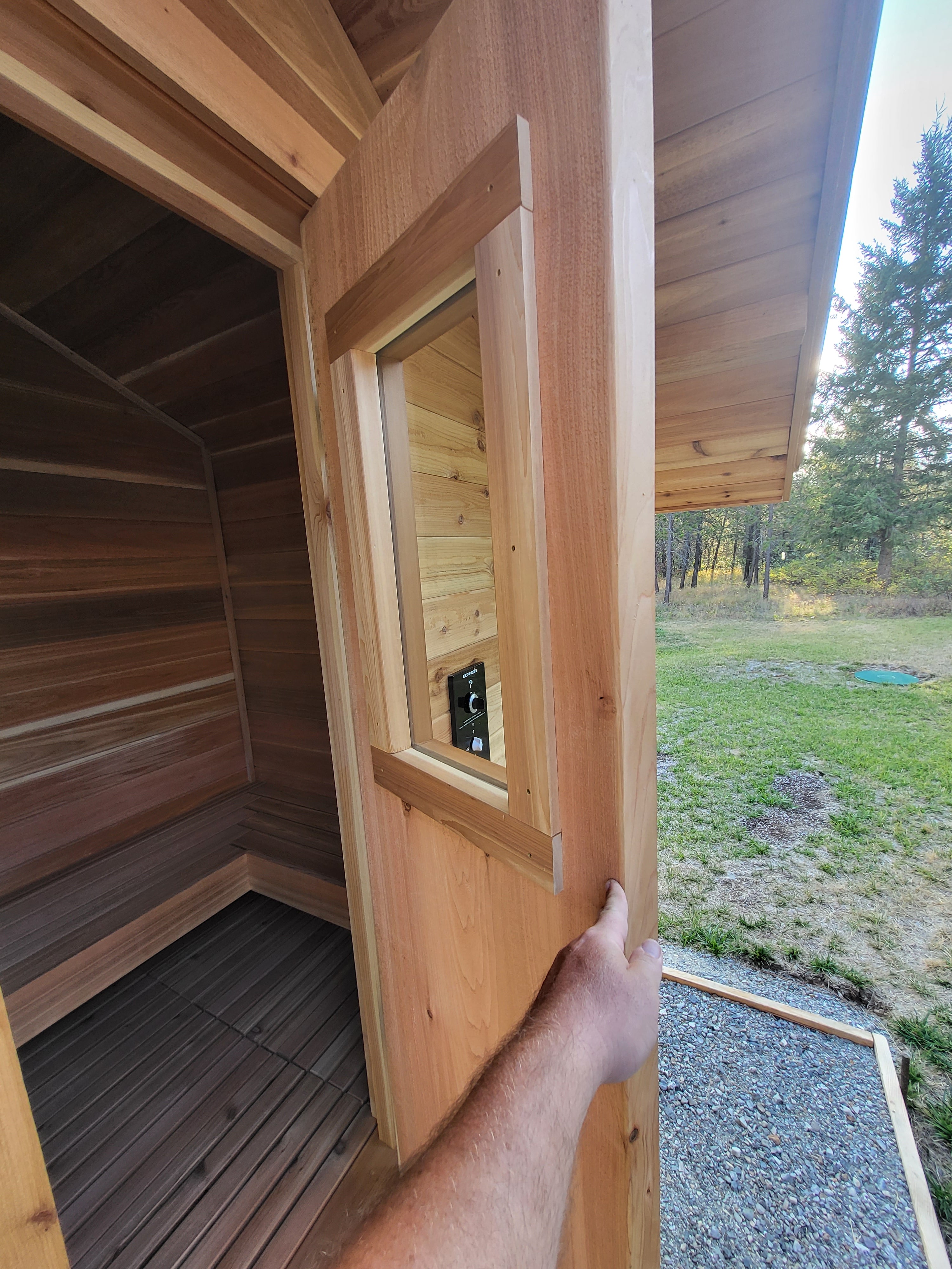 A solid slab sauna door held open reveal the inside of a custom built backyard sauna by Sauna Fauna.
